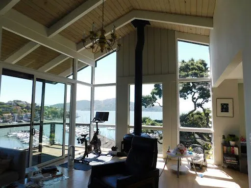 Existing living room before renovation: vaulted wood ceiling, floor-to-ceiling glazing over the bay and marina, exercise bike and toys