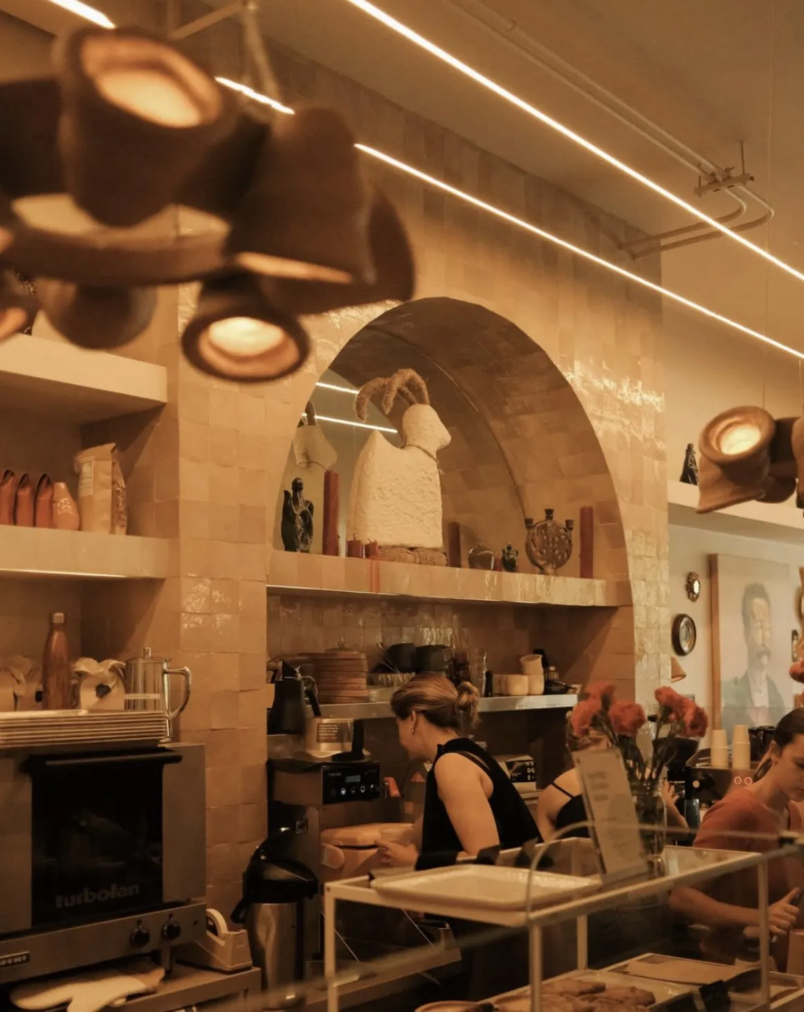 Barista at work beneath the zellige arch and open shelving of ceramics behind the bar