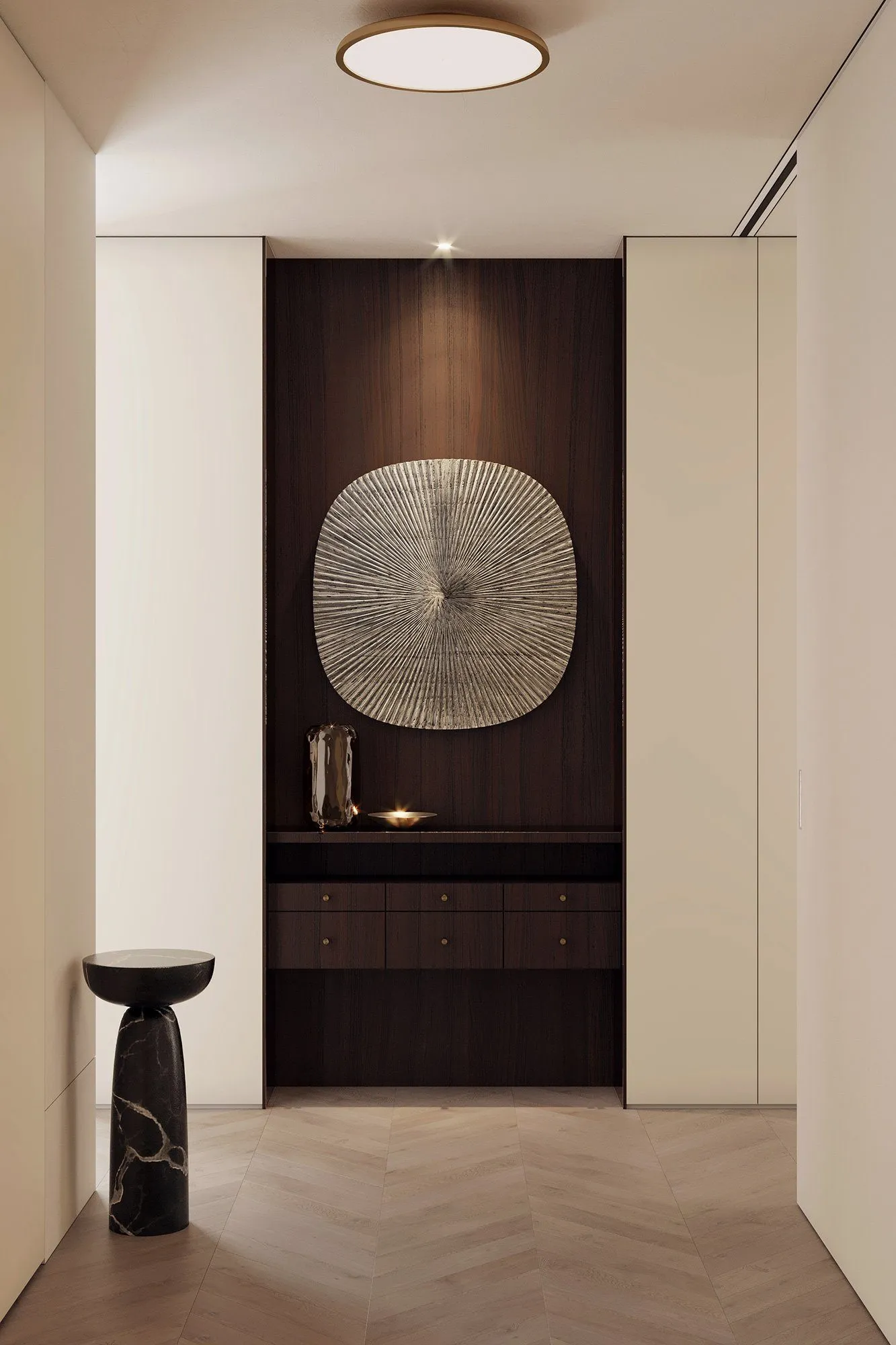 Entry niche in dark walnut with a ribbed silver medallion, sculptural glass vase and black marble pedestal table on chevron oak — Minimalist Glamour - condo