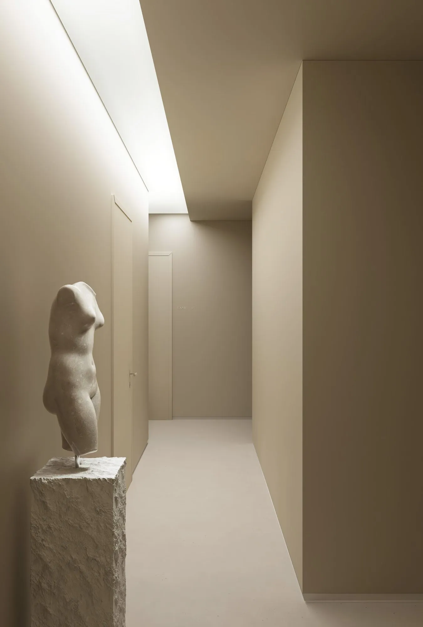 Corridor with classical stone torso sculpture and cove lighting outside exam rooms