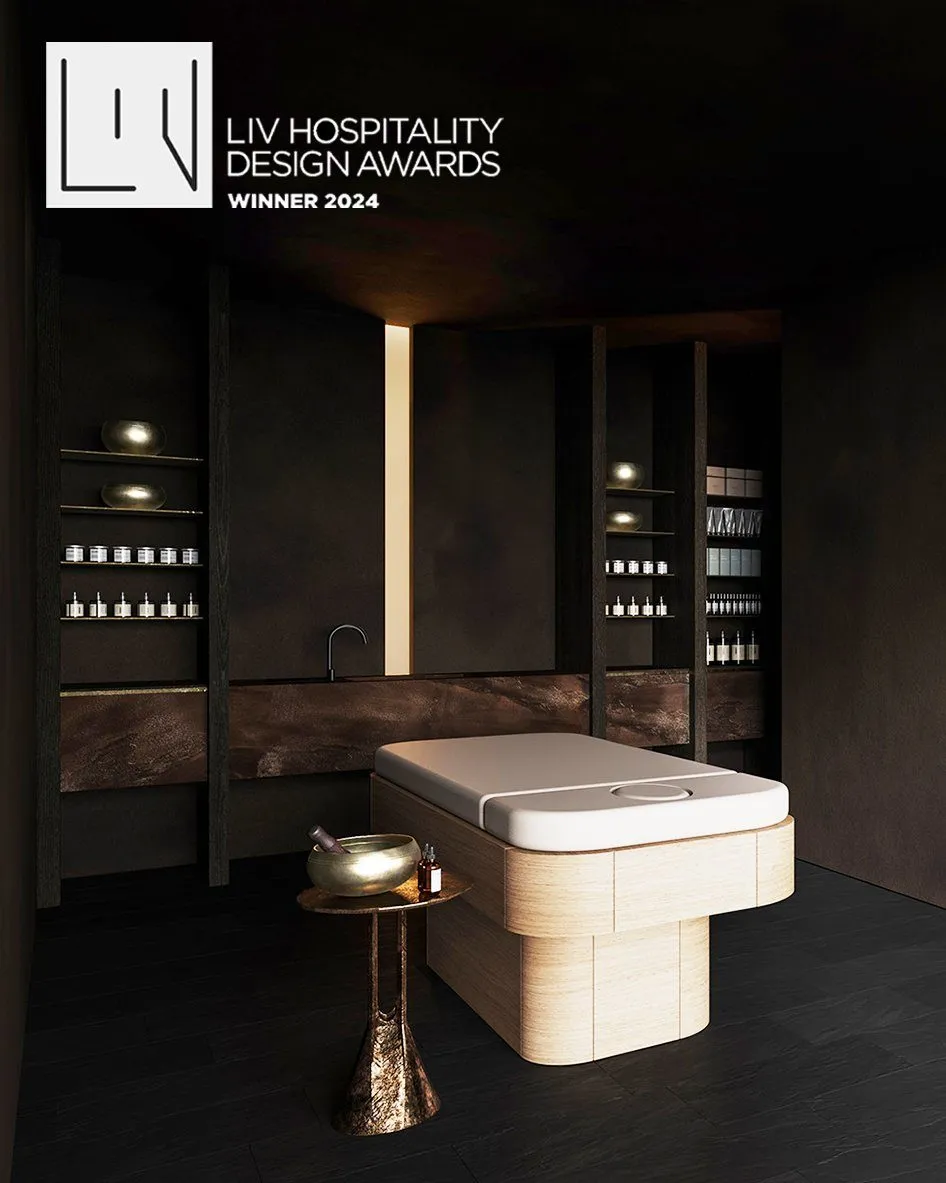 Treatment room in dark plaster with a light-wood massage table and brass singing bowl, bearing the LIV Hospitality Design Awards 2024 winner badge — Obsidian Oasis Spa