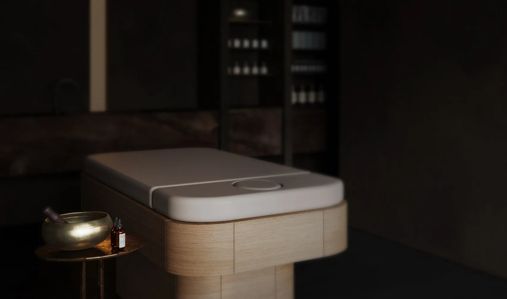 Close view of the pale wood massage table with a brass singing bowl and oil bottle on a hammered-bronze side table — Obsidian Oasis Spa